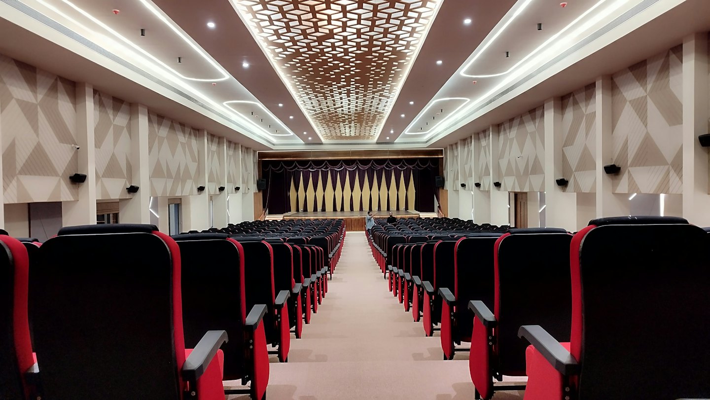 Posti vuoti in un auditorium di fronte a un palco con tende viola e oro.